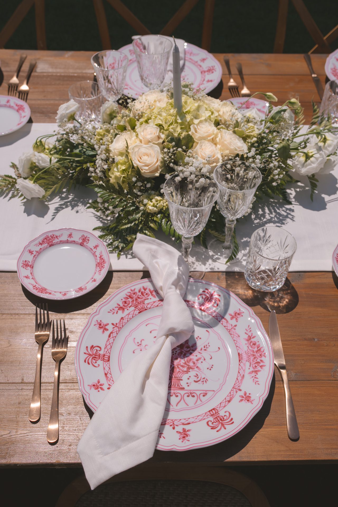 Mise en place in stile rustico toscano con eleganti piatti bianchi decorati in rosso, tovagliolo con fiocco e rose bianche