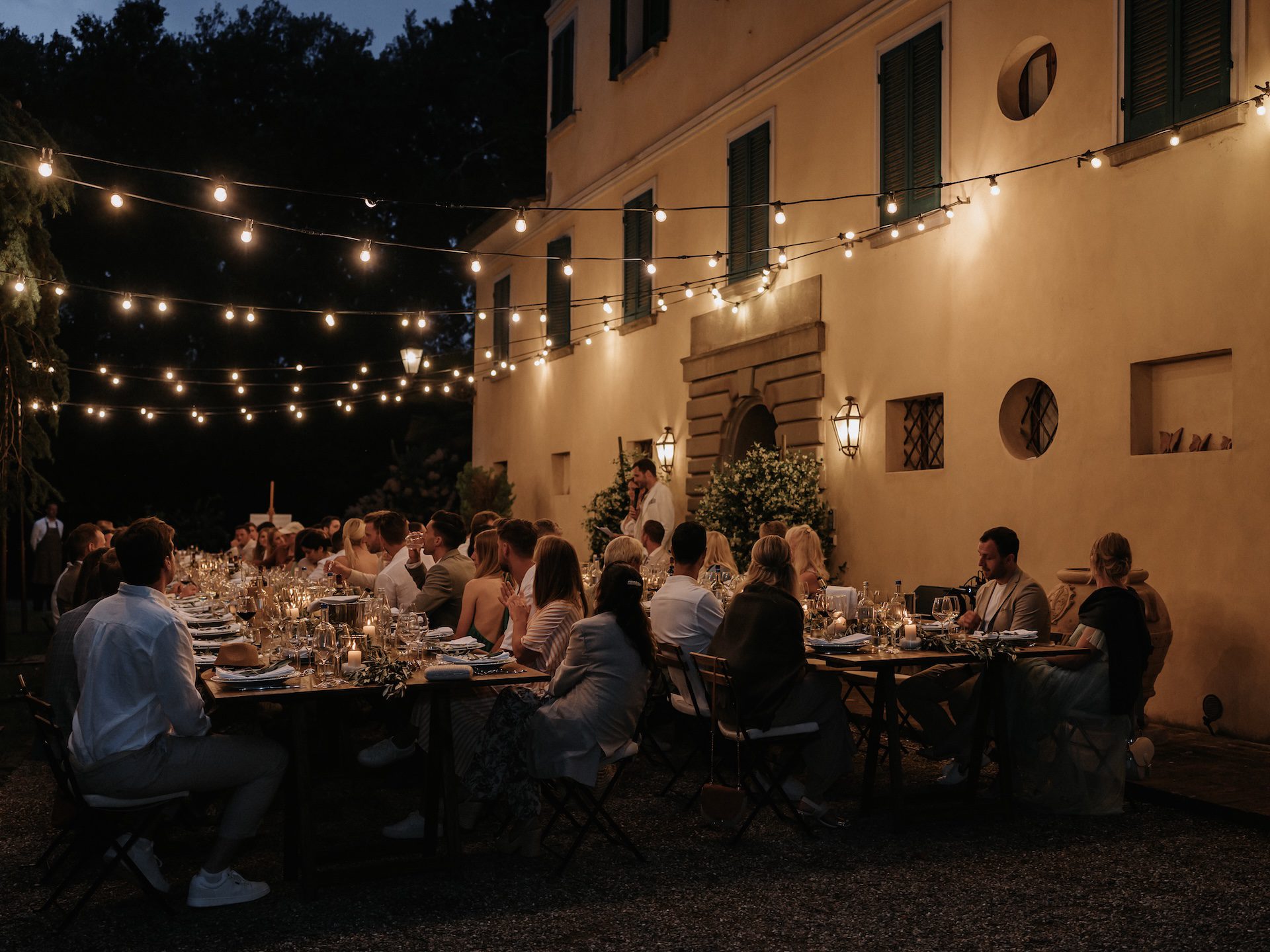 Sposi e invitati a tavola durante la cena di matrimonio con romantiche luci fairy lights